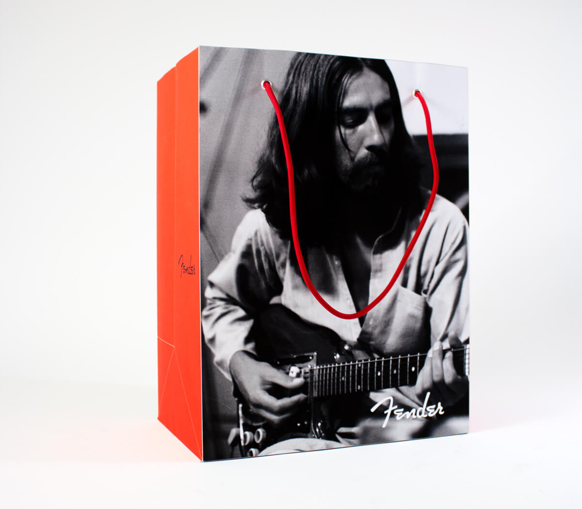 Closeup of a red bag with a photo of George Harrison playing guitar and the Fender logo.